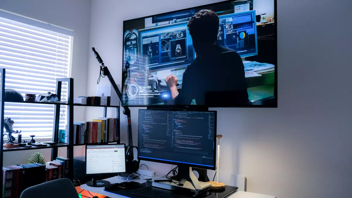 A man is working on a computer, looking at a large screen with AI and data related visual elements, in a well lit office setting.